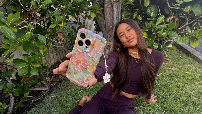 A customer in a garden holding up her floral Bloomy iPhone case